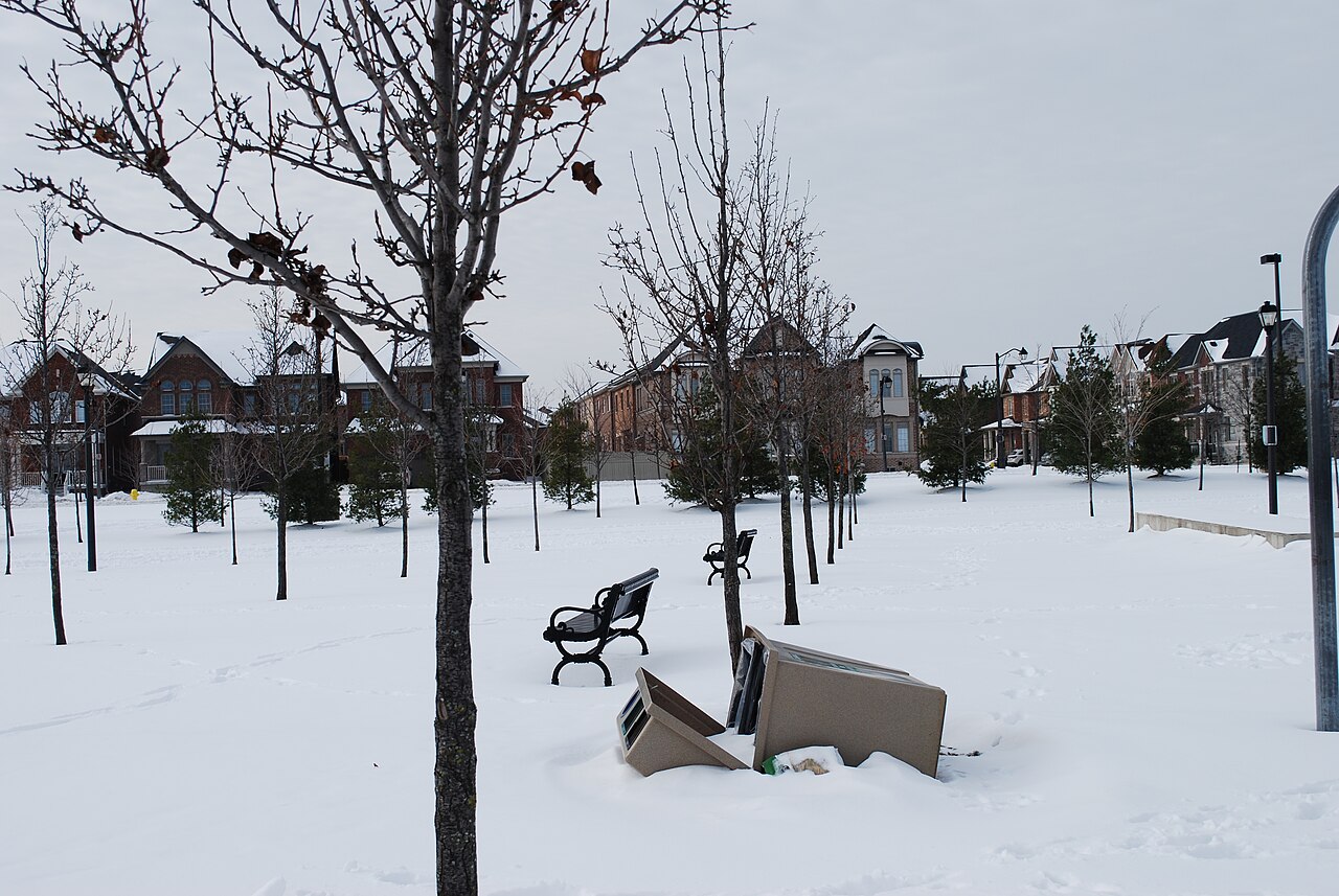 A trash can knocked over and sitting in fresh winter snow